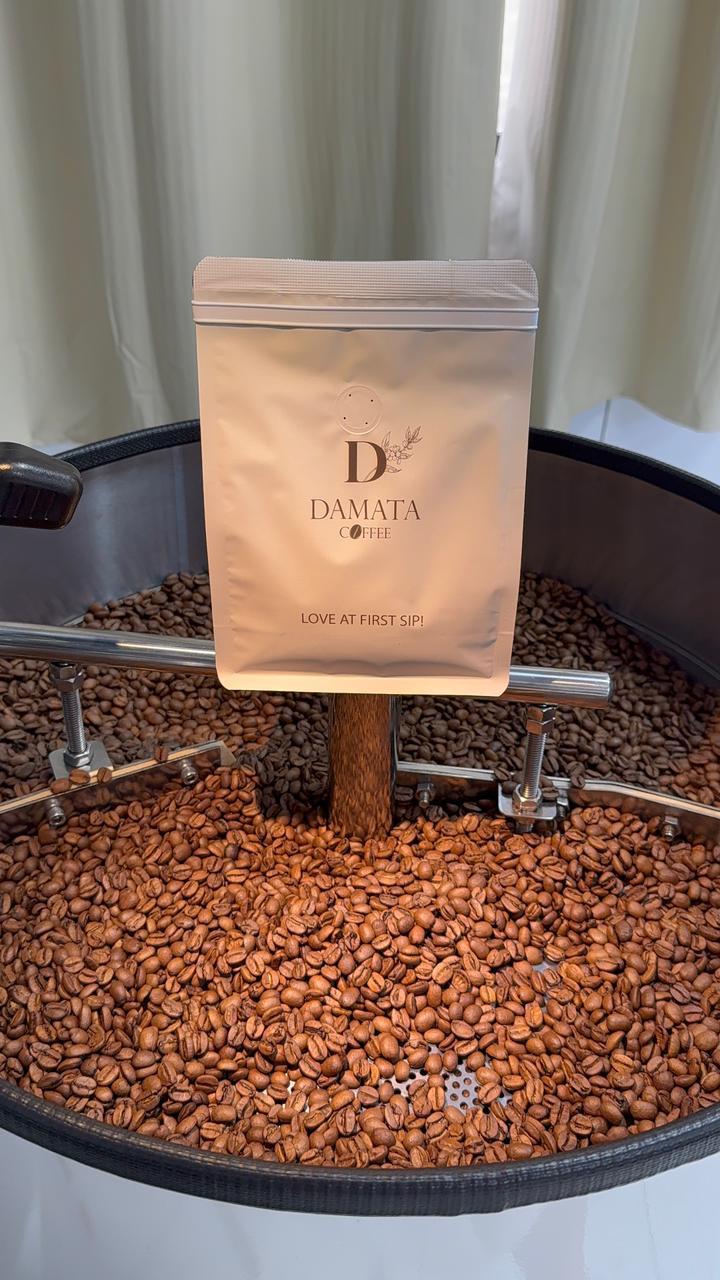 A Damata Coffee bag resting on a tray of freshly roasted beans